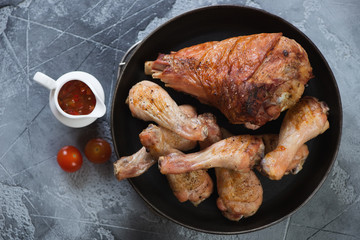 Metal pan with roasted turkey and chicken drumsticks, above view on a grey concrete background, horizontal shot