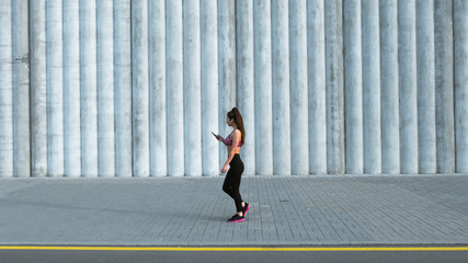 Fototapeta na wymiar Full length shot of fit young woman choosing music before jogging oudside. Fitness model exercising in morning outdoors. Healthy lifestyle concept
