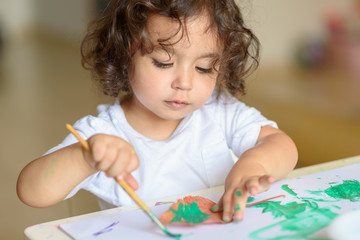 Summer or Autumn.Cute little girl drawing with green paint on fall lives. Curly adorable child...