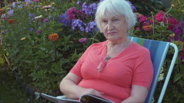 Senior woman reading magazine in garden with flowers outdoor
