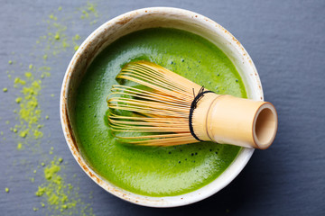 Matcha green tea cooking process in a bowl with bamboo whisk. Black slate background. Top view. © annapustynnikova