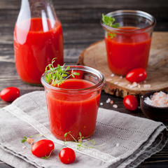 Tomato juice in glass with cress salad, fresh tomatoes on wooden cutting board and grey towel.