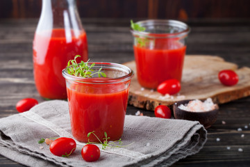Tomato juice in glass with cress salad, fresh tomatoes on wooden cutting board and grey towel.