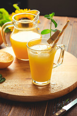 Glass of fresh pressed orange juice with ice cubes and oranges on wooden table. Autumn cozy rustic mood still life