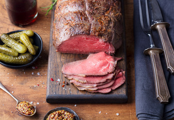 Roast beef on cutting board. Wooden background.