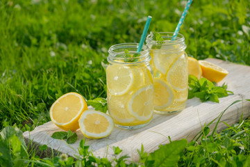 Lemonade in jars of hipster for jam on a background of green grass. Concept: picnic with refreshing drinks