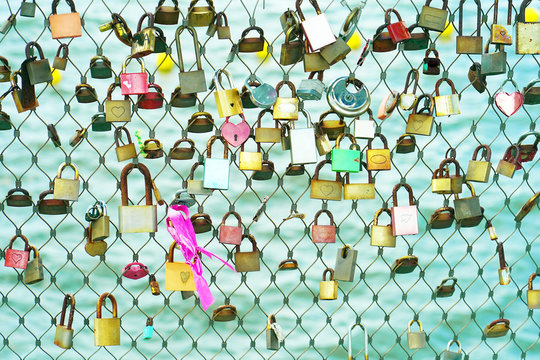 Padlocks of love hangs on the Bridge which is symbol of eternal love bind together. Summer vacation season. Metal grid fence with love locks on the sea background.