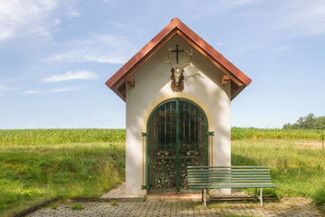 Hunting chapel. Rural wayside shrine in hunting style with deer antler and skull and decorative trellis. Bench by the field. Lower Austria. Burgenland. Central Europe.