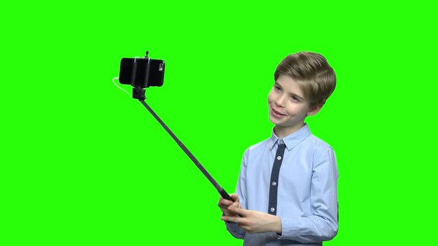 Cute caucasian boy with selfie stick posing for camera. Green hromakey background for keying.