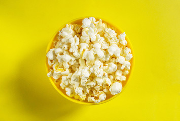 Movie theater popcorn in a bowl on yellow background. Top view 