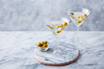 Martini cocktail with green olives on marble table background. Copy space.