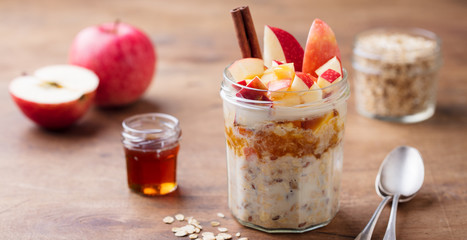 Overnight oats, bircher muesli with apple, cinnamon and honey. Wooden background.