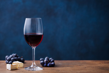 Glass of red wine with fresh grape and cheese on wooden table. Blue background. Copy space. - Powered by Adobe