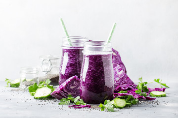 Vegan vegetable smoothie with purple cabbage, cucumber and chia seeds in glass bottles on gray table, selective focus