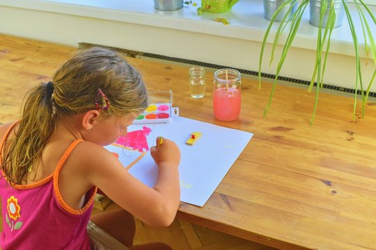 Little girl painting simple picture. Cute girl painting with watercolors. Window background. Selective focus and small DOF