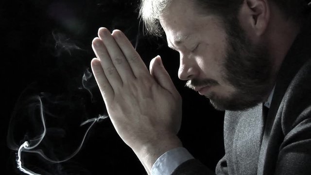 Close up profile shot of a business man in prayer. Strongly backlit shot over black.