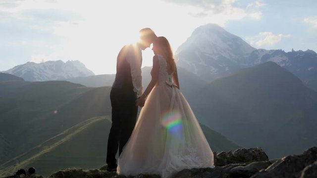 Lovers groom and bride enjoy a wonderful summer evening in the rays of the setting sun against the backdrop of the majestic mountains. Georgia. The concept of a happy family life