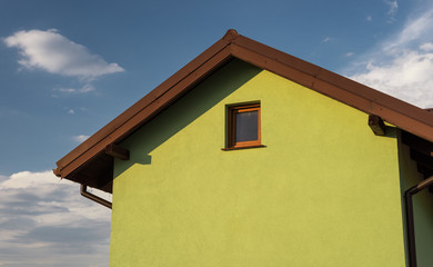 Bright green house facade with visible roof soffit and windows. In the background a nice blue sky with clouds.