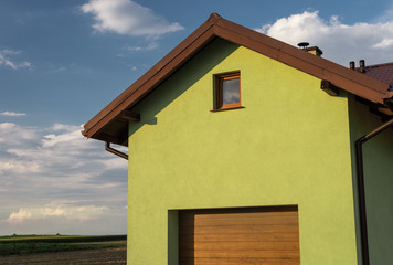 A bright green facade of the house with a visible roof soffit, window and garage door. In the background a nice blue sky with clouds.