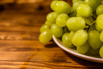 Ceramic plate with green grapes on wooden table