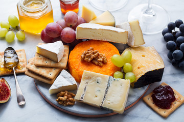 Assortment of cheese, grapes with red and white wine in glasses. Marble background. Top view.
