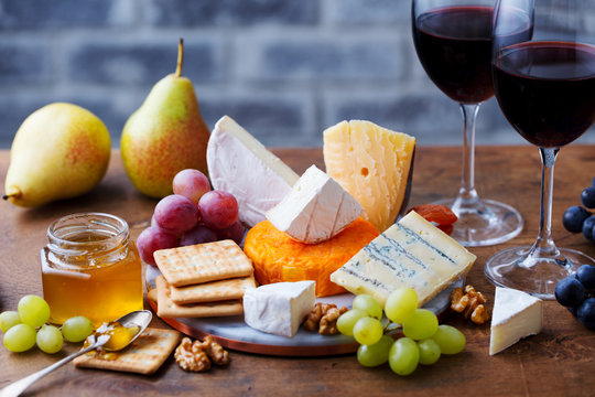 Assortment of cheese, grapes with red wine in glasses. Wooden background.