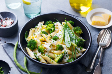 Pasta with green vegetables and creamy sauce in black bowl on grey stone background.