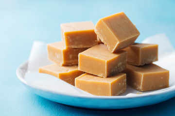 Fresh caramel fudge candies on a plate. Blue background. Close up.