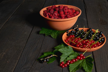 Ceramic plate with black and red currant and bowl of red raspberries on black rough wooden texture table