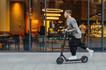 Attractive man riding a kick scooter at cityscape background. © Akaberka