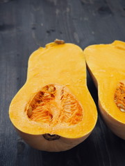 Ripe pumpkin upon dark wooden background, halved. Bottled shaped butternut squash Selective focus. 