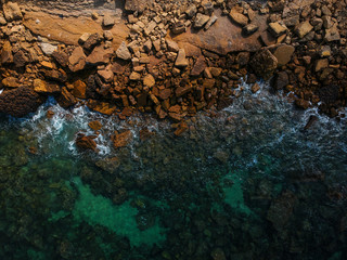 Aerial view of waves, rocks and transparent sea. Summer seascape. Top view from drone. Rocky coastline. 