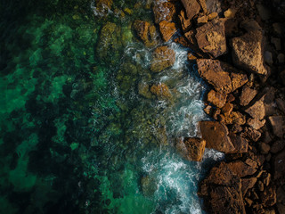 Fototapeta na wymiar Aerial view of waves, rocks and transparent sea. Summer seascape. Top view from drone. Rocky coastline. 