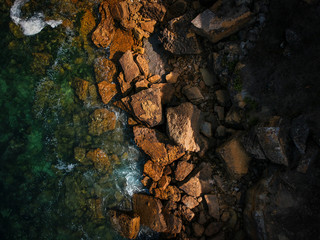 Aerial view of waves, rocks and transparent sea. Summer seascape. Top view from drone. Rocky coastline. 