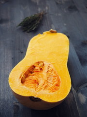 Food background with half of bottle shaped pumpkin and thyme sprigs upon dark vintage table. Selective focus. 
