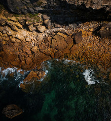 Aerial view of waves, rocks and transparent sea. Summer seascape. Top view from drone. Rocky coastline. 