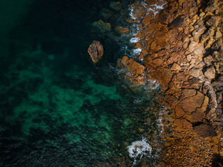 Aerial view of waves, rocks and transparent sea. Summer seascape. Top view from drone. Rocky coastline. 