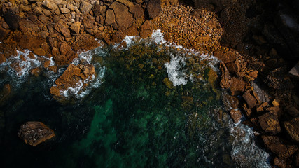 Aerial view of waves, rocks and transparent sea. Summer seascape. Top view from drone. Rocky coastline. 