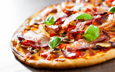 Pizza with Mozzarella cheese, mushrooms, bacon, Tomatoes, pepper, Spices and Fresh Basil. Italian pizza on wooden background.