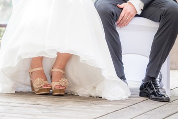 Fototapeta na wymiar Braut Bräutigam sitzen bei Hochzeit und Trauung nebeneinander. Mann und Frau tragen Luxus Hochzeitskleid, Anzug und Schuhe. Das Mädchen zeigt Füsse mit Nagellack. Der schwarze Schuh ist poliert