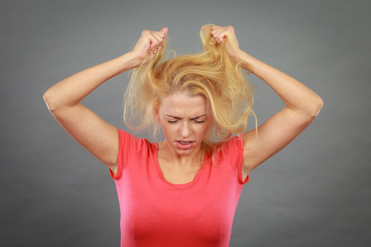 Frustrated woman holding her damaged blonde hair