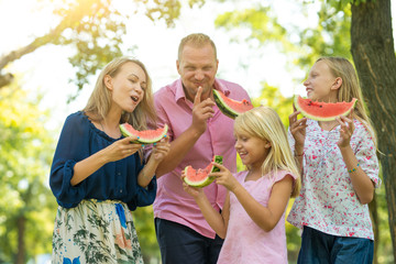 Young family with children having fun in nature eating watermelon