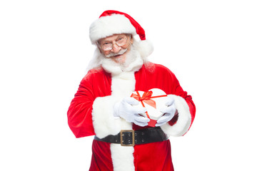 Christmas. Smiling Santa Claus in white gloves holds a red and white heart-shaped gift box with a red ribbon. Isolated on white background.