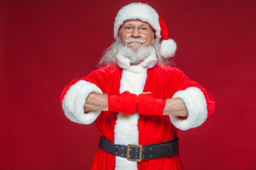 Christmas. Santa Claus with red bandages wound on his hands for boxing imitates kicks. Kickboxing, karate, boxing. Isolated on red background.