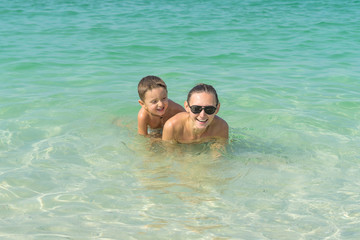 Fototapeta premium Happy smiling family having fun on tropical white beach (Maldives islands). Mother and cute son. Positive human emotions, feelings, joy. Spring, summer and winter holidays.