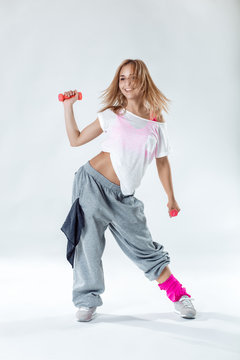 Young beautiful slim fitness girl with weight dancing on a white studio background