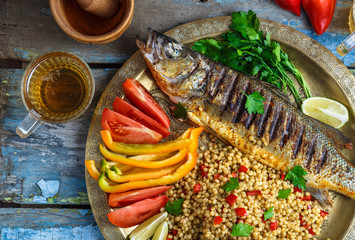 Close view of grilled sea bass with vegetables and ptitim, middle eastern cuisine