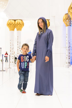 Woman with cute son dreaming at the grand mosque of Sheikh Zayed Mosque in Abu Dhabi wearing abaya, paranja in night time. Travelling.