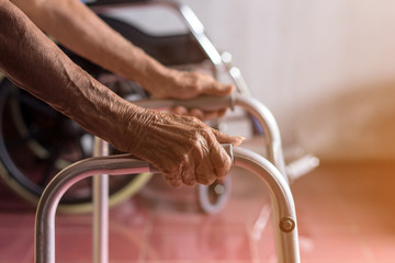 Asian old woman standing with her hands on a walker stand,Hand of patient woman holding a walking aid