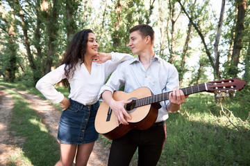 young couple walking in the forest, playing guitar and dancing, summer nature, bright sunlight, shadows and green leaves, romantic feelings